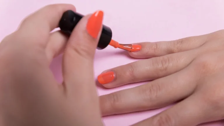 Hand mit korallfarbenen Gelnägeln und Nagellackflasche – Nageldesign in Berlin